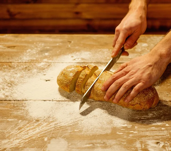 Uomo che taglia pane fatto in casa su un tavolo — Foto Stock