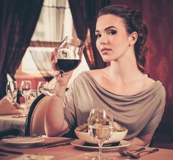 Young woman with glass of red wine alone in a restaurant — Stock Photo, Image