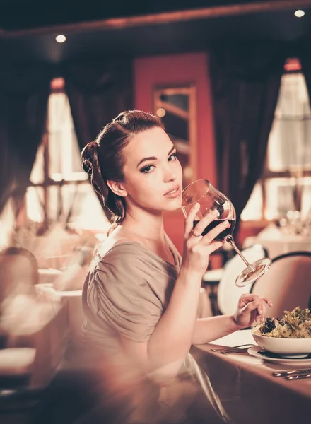 Νεαρή γυναίκα με ποτήρι κόκκινο κρασί, μόνο σε ένα εστιατόριο — Φωτογραφία Αρχείου