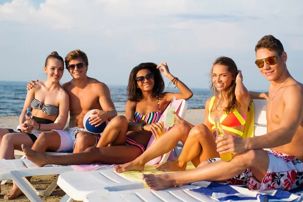 Group of multi ethnic friends with drinks relaxing on a beach — Stock Photo, Image