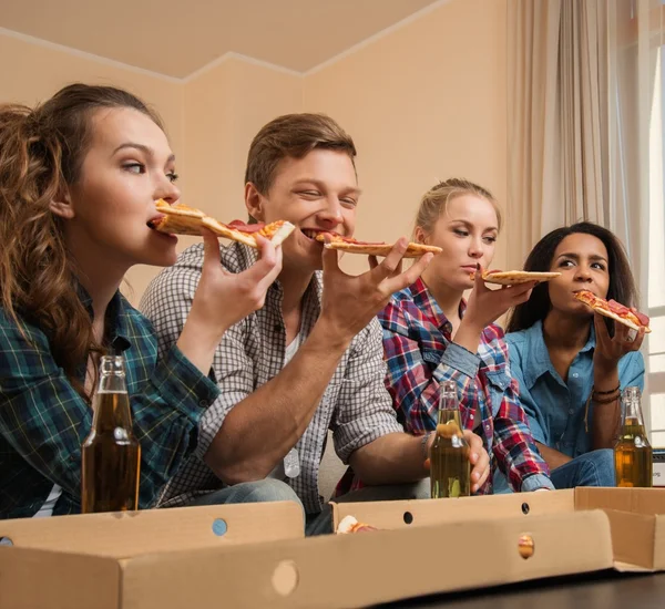 Grupo de jóvenes amigos multiétnicos con pizza y botellas de bebida celebrando en el interior del hogar — Foto de Stock