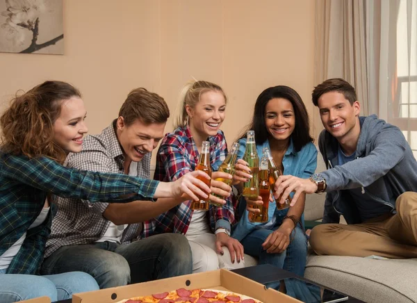 Grupp unga multietniska vänner med pizza och flaskor med drink firar i heminredning — Stockfoto