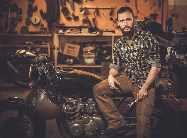 Rider and his vintage style cafe-racer motorcycle in customs garage — Stock Photo, Image