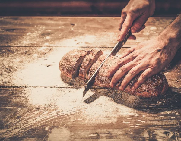 Uomo che taglia pane fatto in casa su un tavolo — Foto Stock