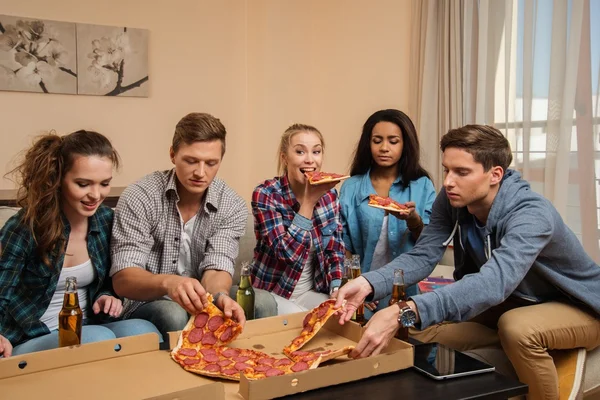 Grupo de jóvenes amigos multiétnicos con pizza y botellas de bebida celebrando en el interior del hogar — Foto de Stock