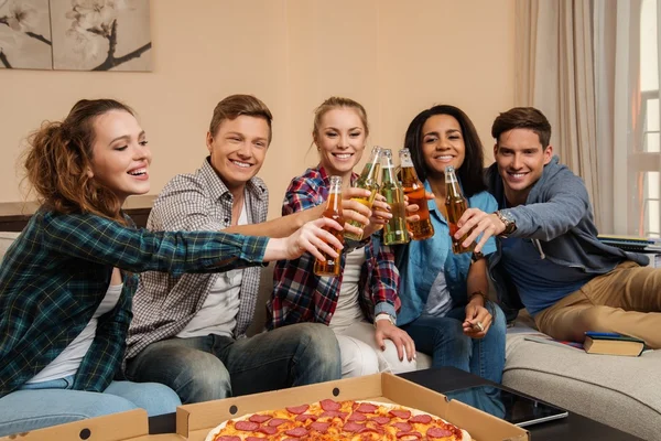 Группа молодых многонациональных друзей с пиццей и бутылками напитков празднуют в интерьере дома — стоковое фото