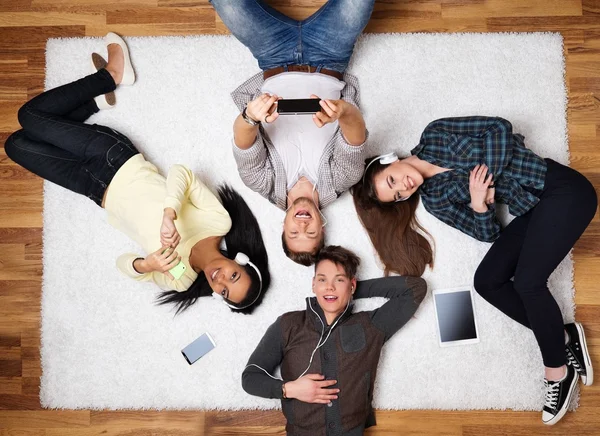 Felices amigos multirraciales relajándose en una alfombra con gadgets —  Fotos de Stock