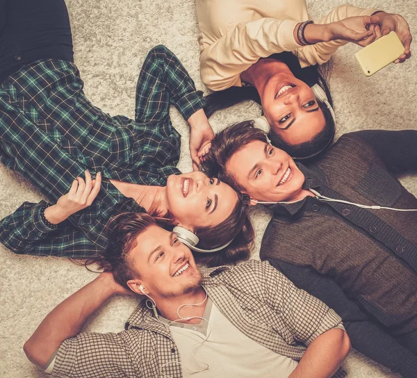 Felices amigos multirraciales relajándose en una alfombra con gadgets — Foto de Stock