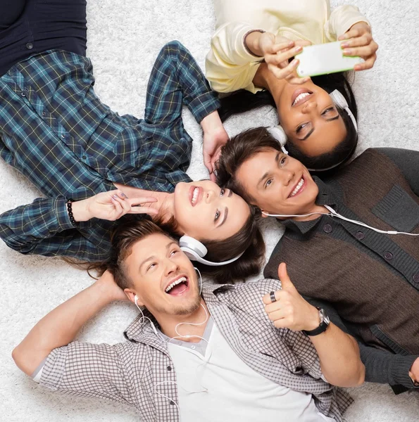 Amigos multirraciais felizes relaxando em um tapete com gadgets — Fotografia de Stock