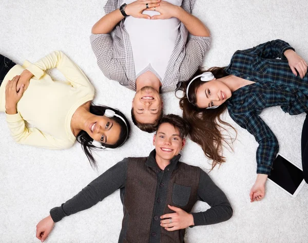 Счастливые многорасовые друзья отдыхают на ковре с гаджетами — стоковое фото