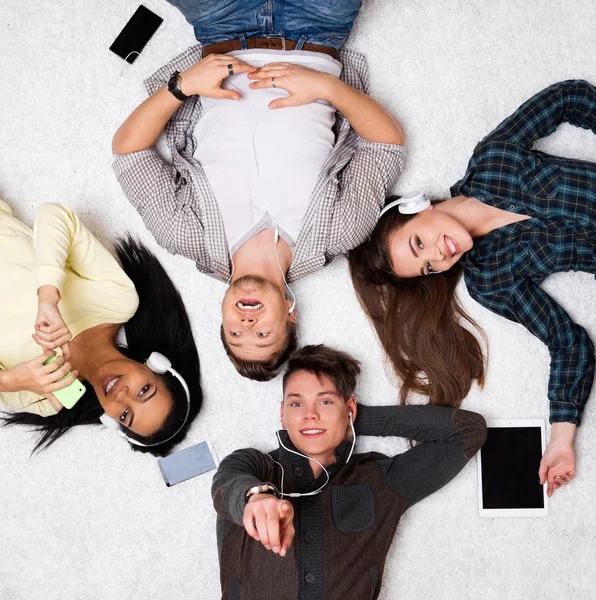 Happy multiracial friends relaxing on a carpet with gadgets — Stock Photo, Image