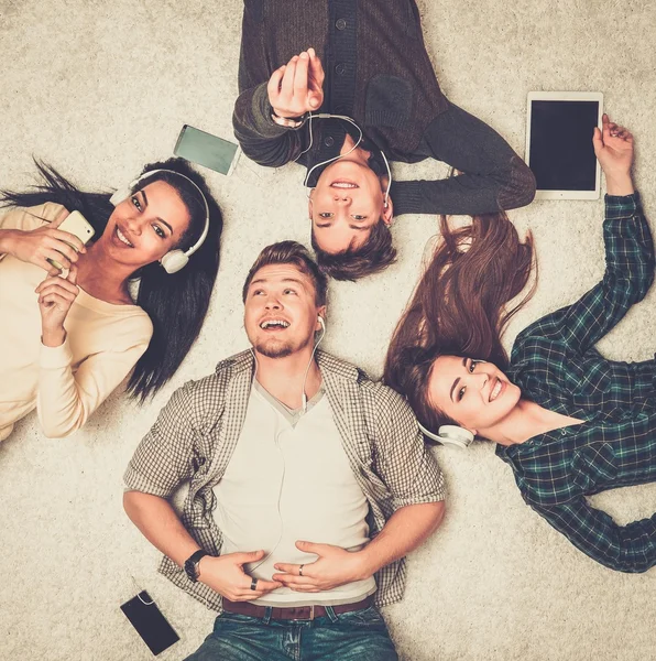 Amigos multirraciais felizes relaxando em um tapete com gadgets — Fotografia de Stock