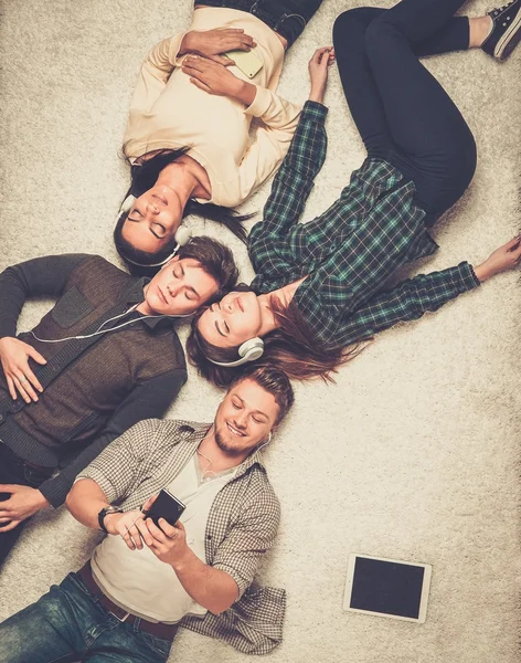 Amigos multirraciais felizes relaxando em um tapete com gadgets — Fotografia de Stock