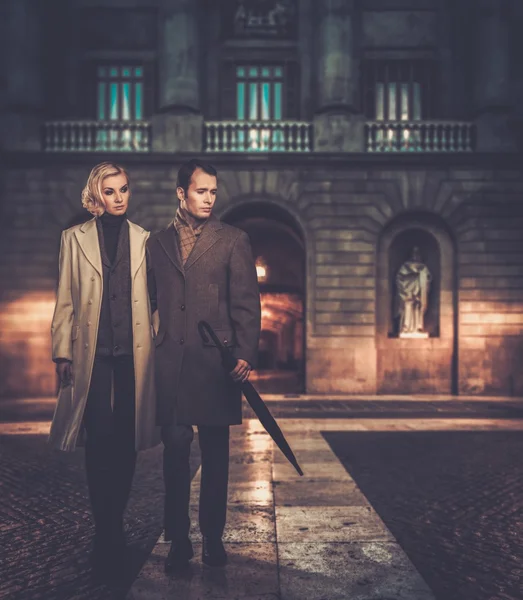 Elegante pareja de abrigos contra la fachada del edificio por la noche —  Fotos de Stock