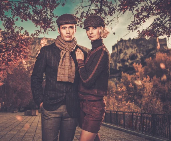 Elegant couple in caps against autumnal landscape — Stock Photo, Image