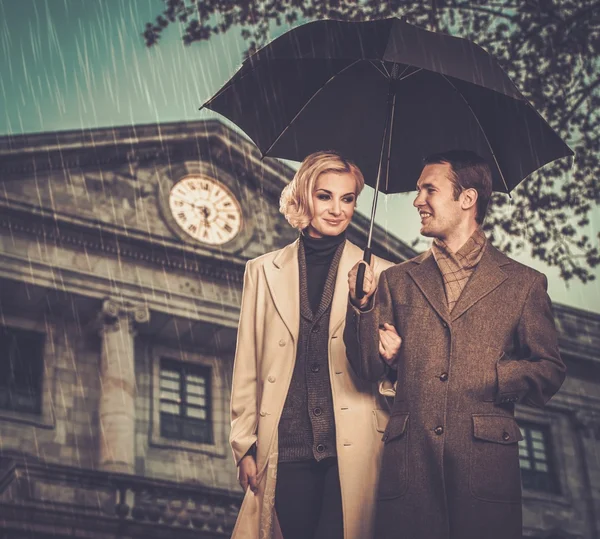 Casal elegante com guarda-chuva contra fachada de construção — Fotografia de Stock