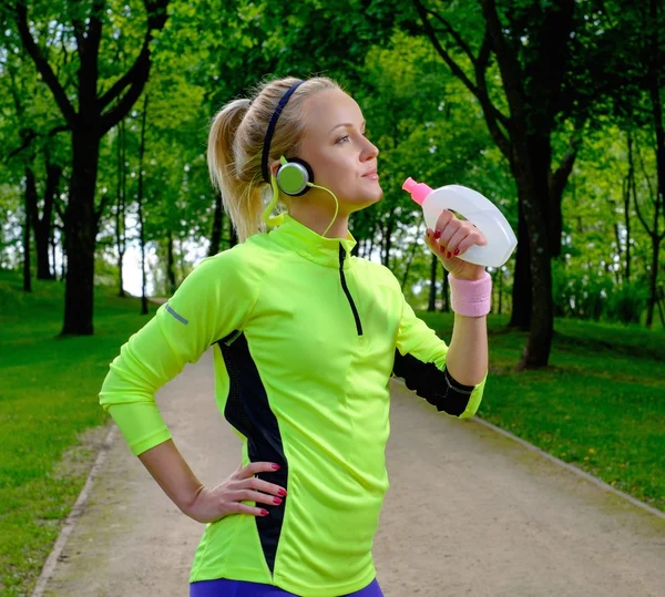 Mulher sorridente desportiva em um parque com garrafa de bebida — Fotografia de Stock