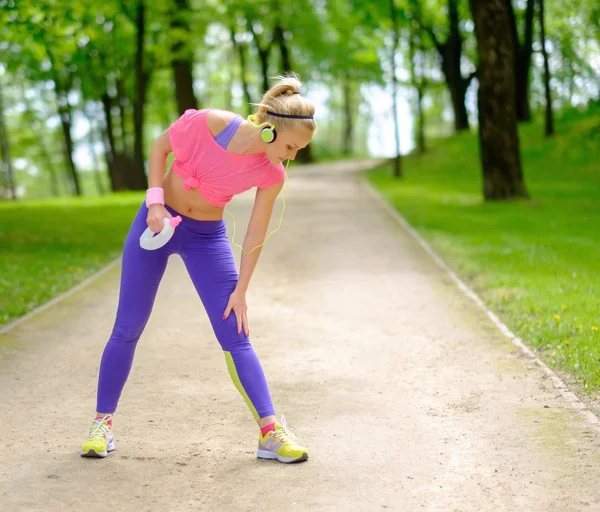 Mulher sorridente desportiva em um parque com garrafa de bebida — Fotografia de Stock