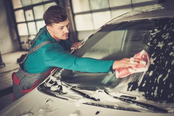 Hombre trabajador lavando parabrisas con esponja en un lavado de coches — Foto de Stock