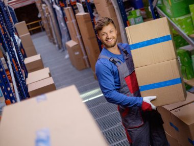 Porter carrying boxes in a warehouse  clipart