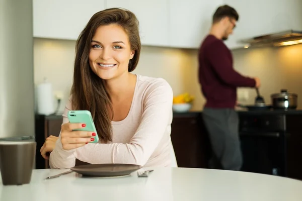 Mulher com telefone celular esperando por comida em uma cozinha em casa — Fotografia de Stock