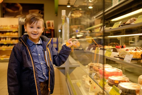 Pequeño niño cerca de la exhibición con pasteles en una tienda de comestibles — Foto de Stock