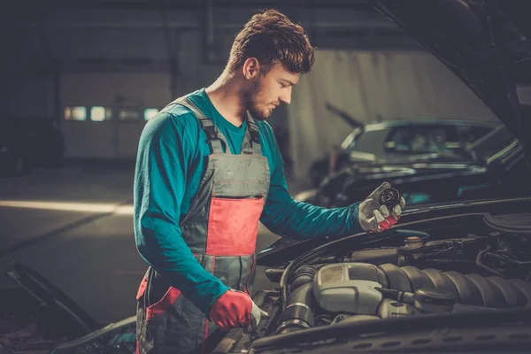 Mechanic with oil filling cork near open hood in a workshop — Stock Photo, Image