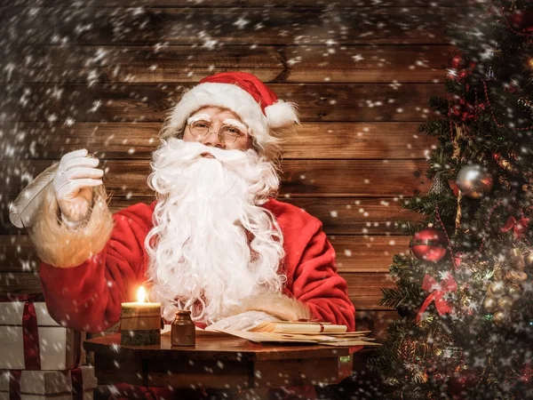 Santa Claus in wooden home interior sitting behind table — Stock Photo, Image