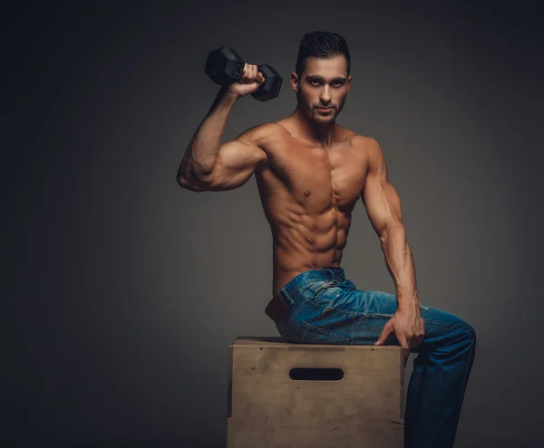 Man in a jeans holding a dumbbell. — Stock Photo, Image