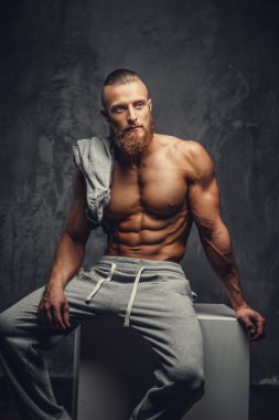 Gri bir arka plan üzerinde poz sakallı gömleksiz kaslı adam.