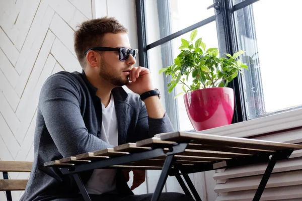 Un hombre con gafas de sol sentado a la mesa . — Foto de Stock