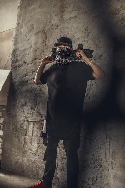Людина в масці тримає пістолет і скейтборд — стокове фото