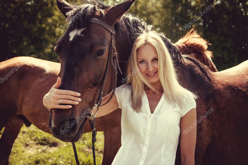 Mujer rubia posando con los caballos marrones — Foto de stock