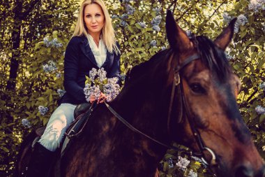 At sırtına oturan sarışın kadın.