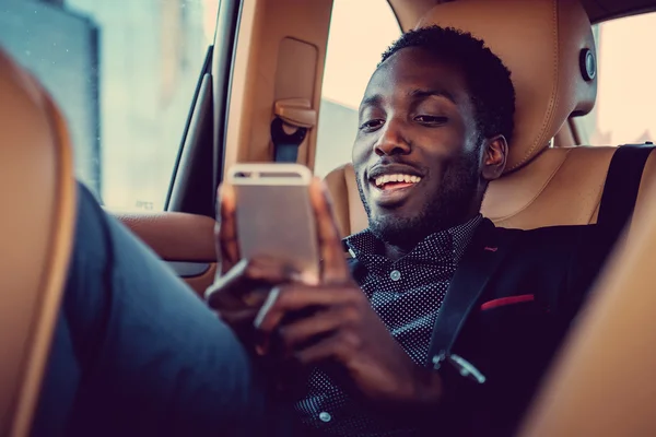 Hombre negro sonriente usando teléfono inteligente —  Fotos de Stock