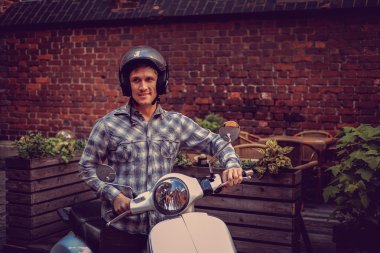 Bir adam eski şehirde beyaz moto scooter üzerinde.