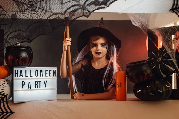 Cheerful preschool girl sitting at halloween stand — Stock Photo, Image