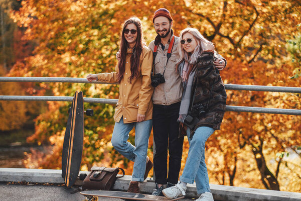 Joyful guy and two girls embracing in autumn forest background