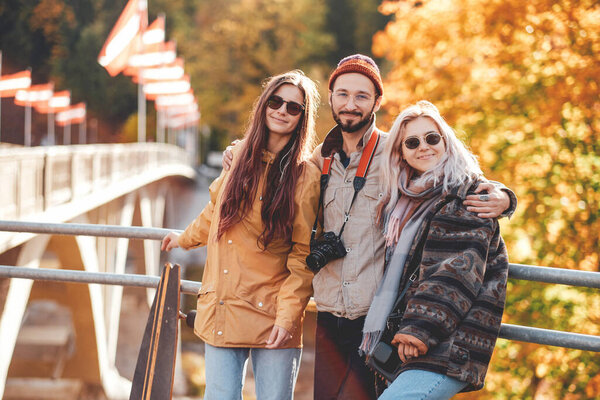 Guy and two pretty girls posing on bridge in autumn park