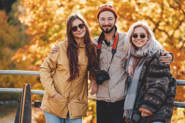 Joyful guy and two girls embracing in autumn forest background