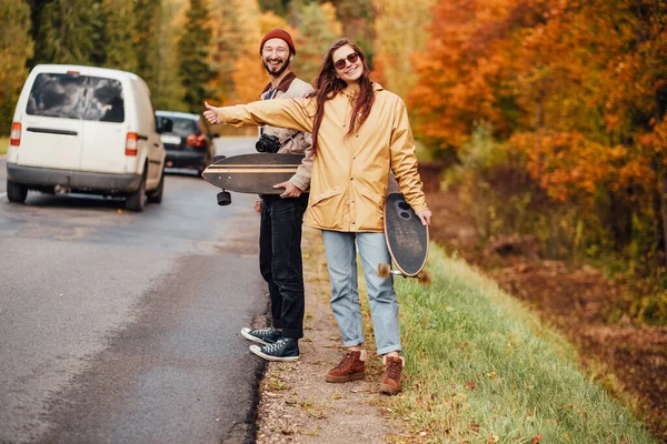 Couple of girl and guy hitchhiking in autumn forest — Stock Photo, Image