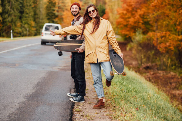 Couple of girl and guy hitchhiking in autumn forest