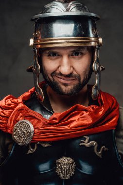 Karanlık arka planda kameraya bakan neşeli Romalı savaşçı.