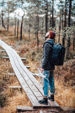 Sakallı adam kalıyor ve ağaçtan yola bakıyor.