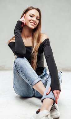 Gülen kız beyaz arka planda yerde oturup kameraya bakıyor.