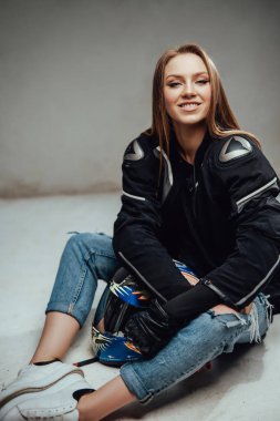 Neşeli bayan motorcu kaskıyla yerde oturuyor.