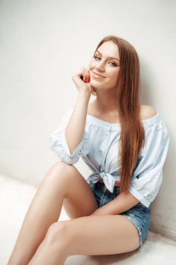 Neşeli kız, eli çenesinin altında, duvarın yanında poz veriyor.