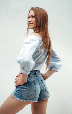 Neşeli kız şortla poz veriyor ve gömleği beyaz arka planda.