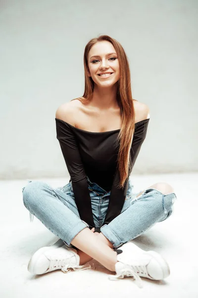 Smiley menina senta-se no chão em fundo branco olhando para a câmera — Fotografia de Stock