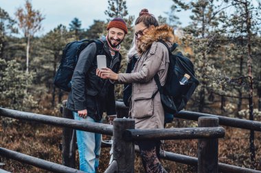 Ahşap platformda akıllı telefona bakan neşeli öğrenciler